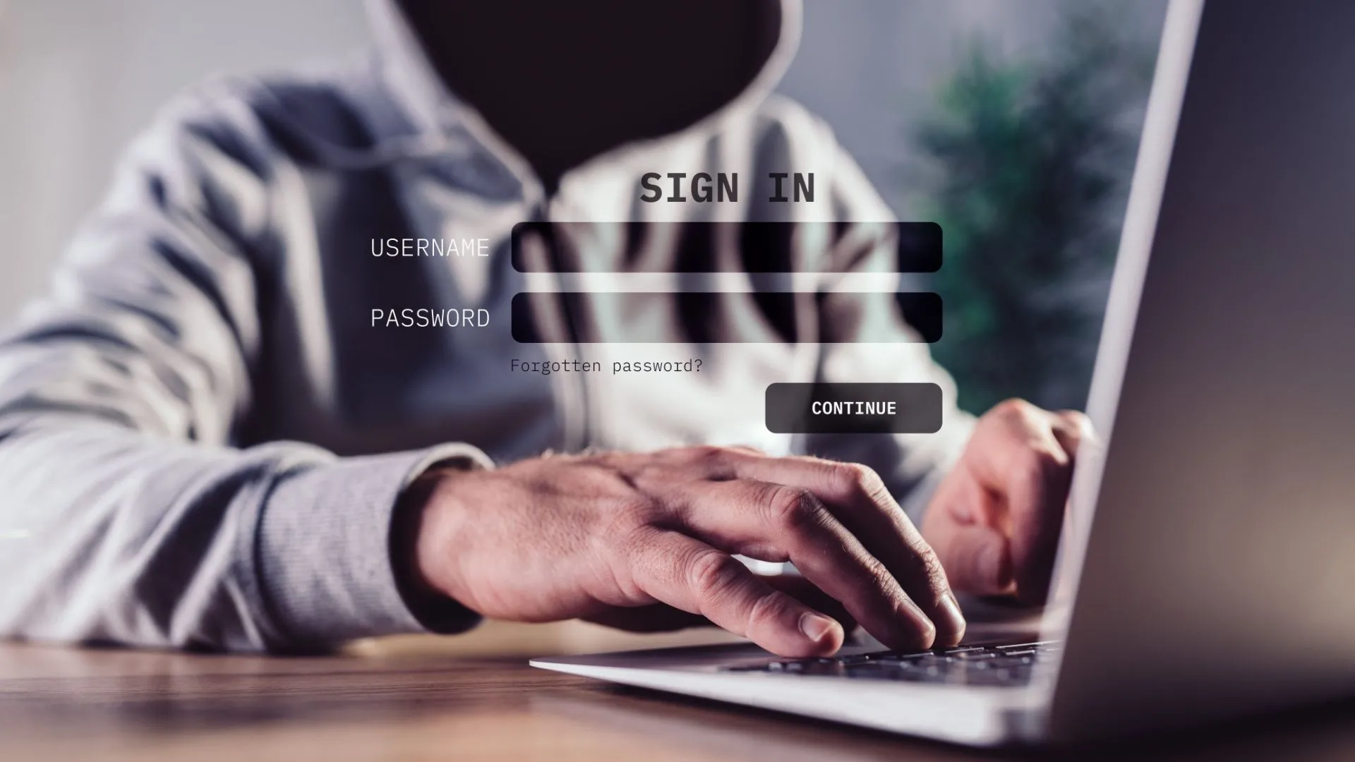 Hacker đội mũ trùm dùng laptop trong bóng tối, biểu tượng rủi ro an ninh